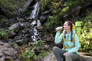 Photo of Tourist with vacuum flask near waterfall in mountains. Space for text
