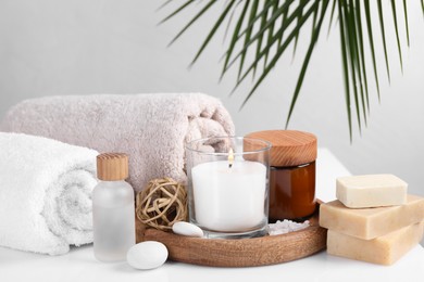 Composition with spa supplies on white table and palm leaf