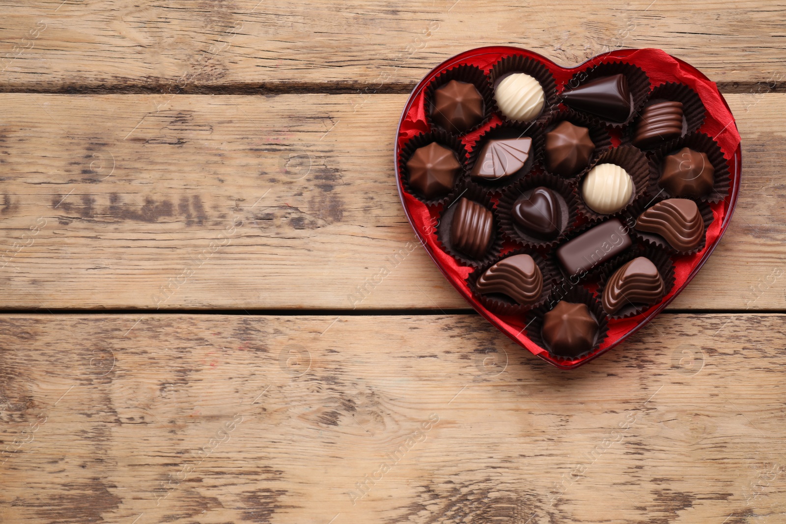 Photo of Heart shaped box with delicious chocolate candies on wooden table, top view. Space for text