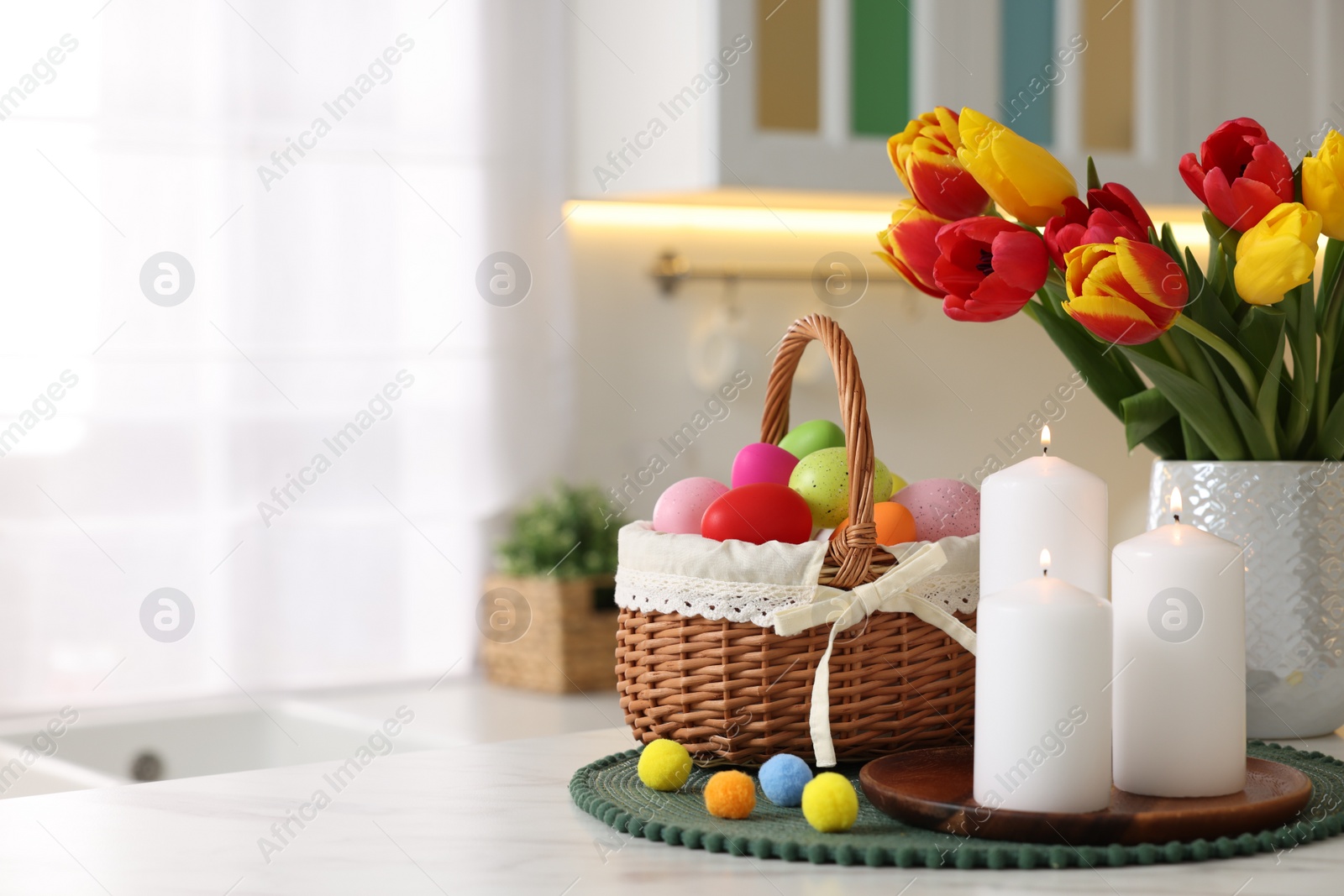 Photo of Easter decorations. Bouquet of tulips, painted eggs and burning candles on table indoors, closeup. Space for text