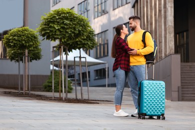 Photo of Long-distance relationship. Beautiful couple with luggage hugging outdoors