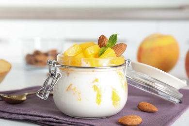 Photo of Tasty peach dessert with yogurt in glass jar on table