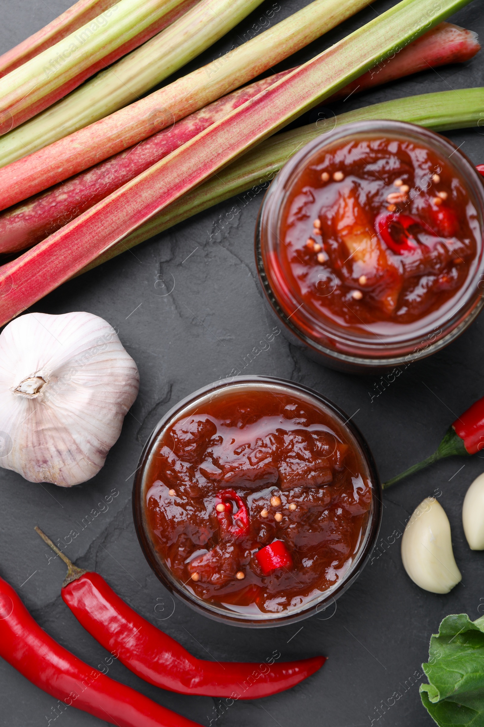 Photo of Tasty rhubarb sauce and ingredients on wooden table, flat lay