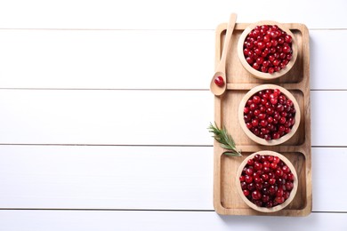 Photo of Fresh ripe cranberries in bowls and rosemary on white wooden table, top view. Space for text