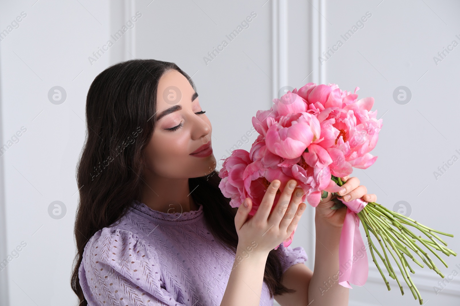 Photo of Beautiful young woman with bouquet of pink peonies near white wall