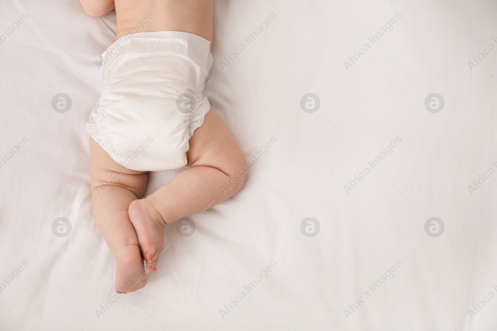 Photo of Little baby in diaper on bed, top view. Space for text