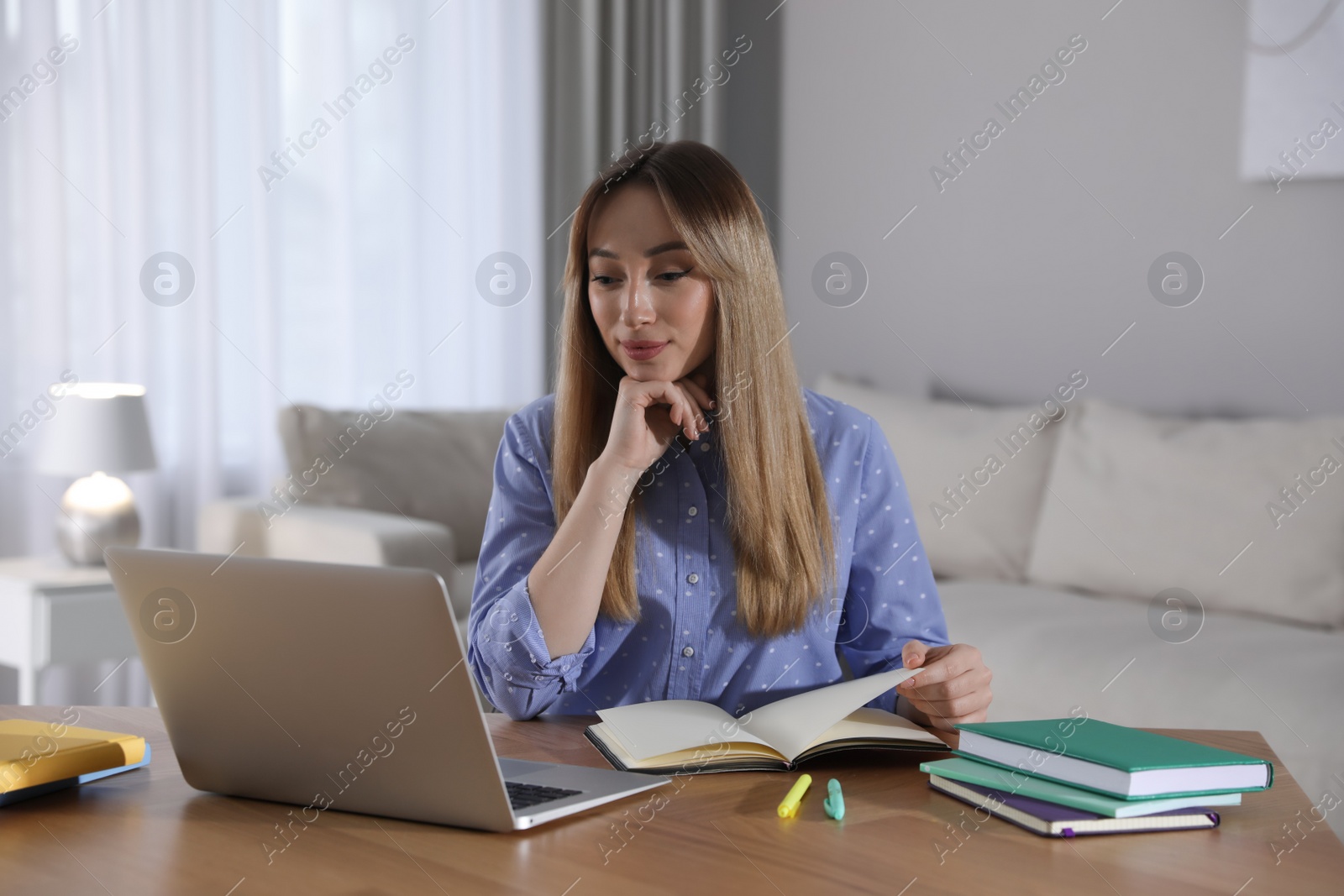 Photo of Young woman watching webinar at table in room