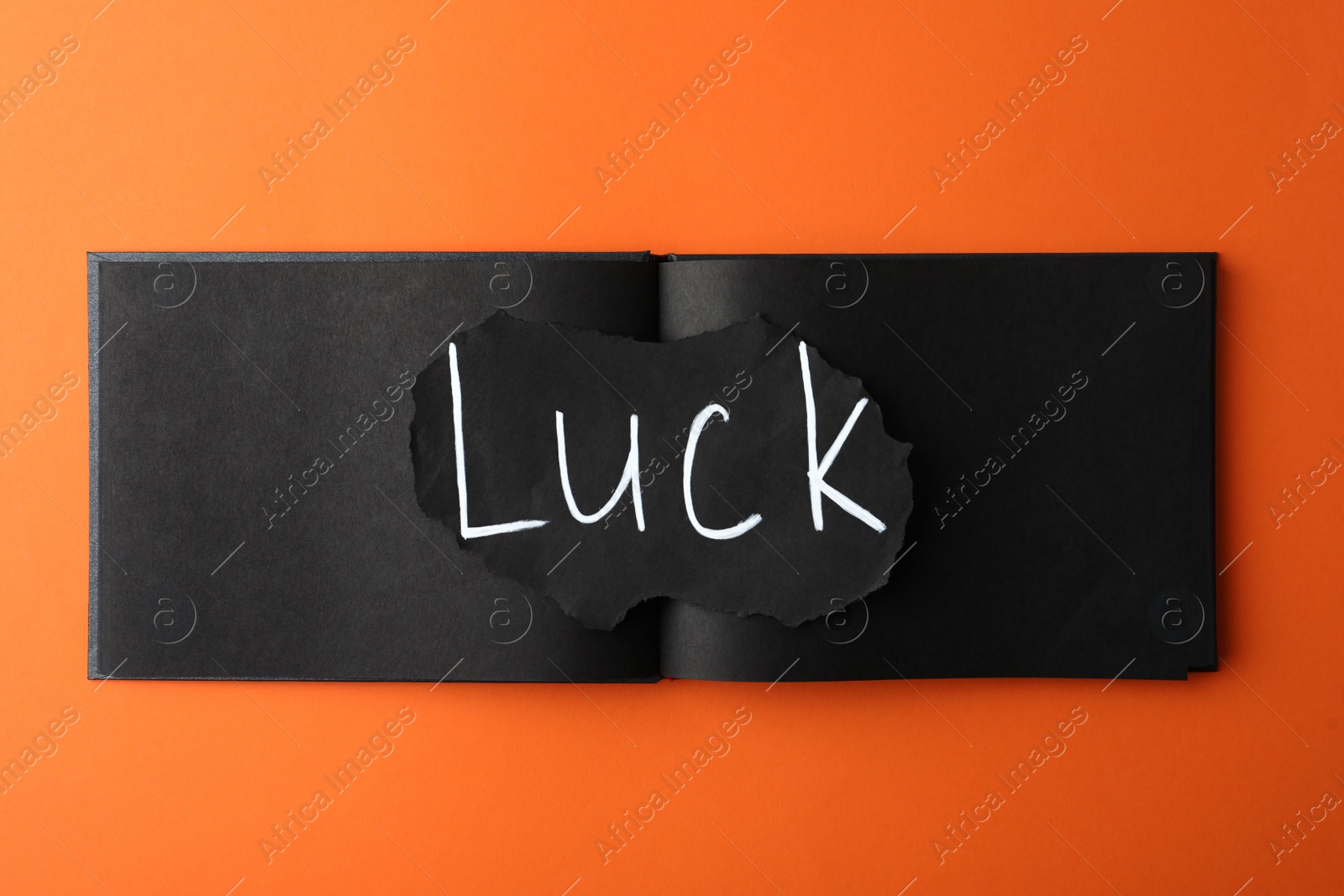 Photo of Sheet of paper with word LUCK and notebook on orange background, top view