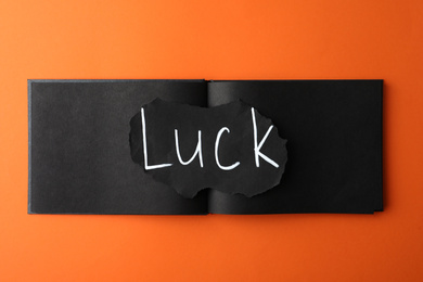 Sheet of paper with word LUCK and notebook on orange background, top view