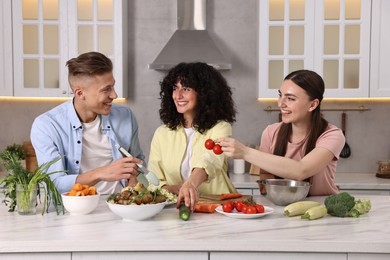 Photo of Friends cooking healthy vegetarian meal at white marble table in kitchen