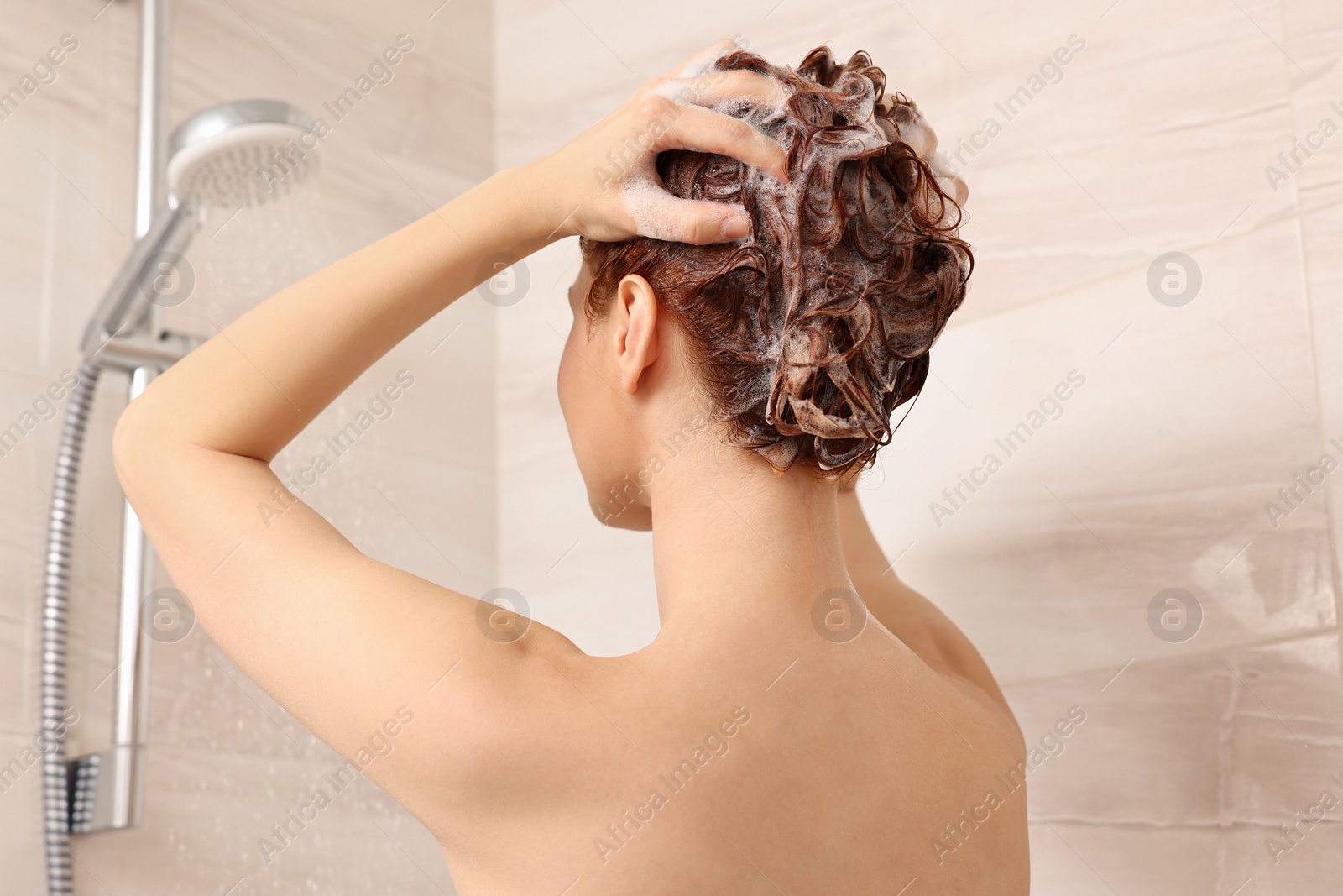 Photo of Young woman washing her hair with shampoo in shower, back view