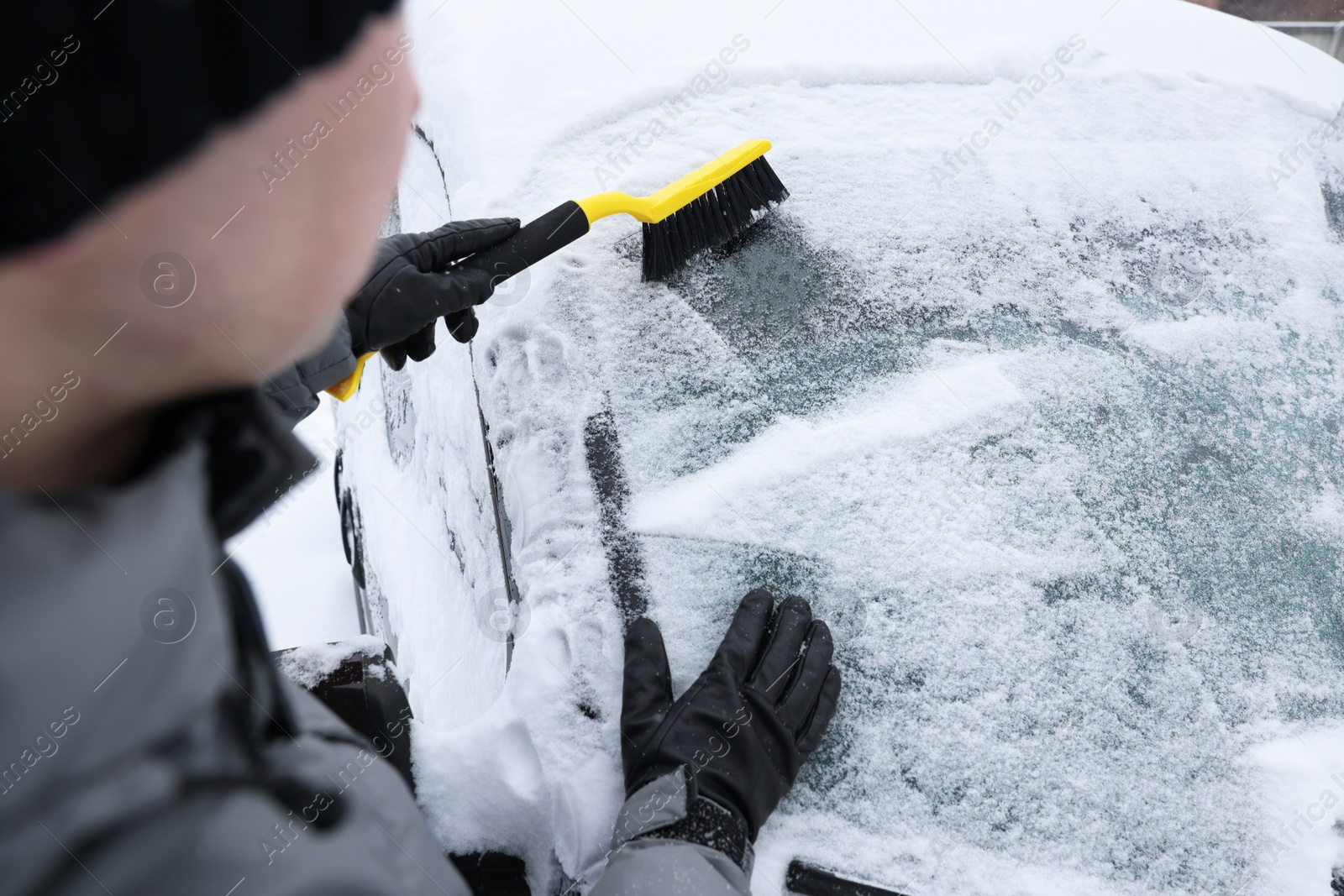 Photo of Man cleaning snow from car windshield outdoors, closeup