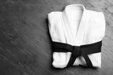 Photo of Martial arts uniform with black belt on grey stone background, top view. Space for text