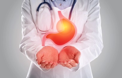 Image of Treatment of heartburn and other gastrointestinal diseases. Doctor holding stomach illustration on grey background, closeup