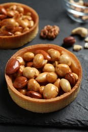 Photo of Tartlets with caramelized nuts on black slate, closeup. Delicious dessert