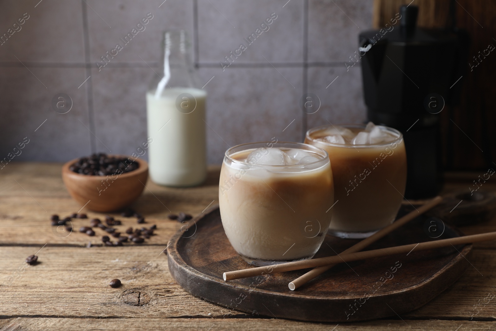 Photo of Refreshing iced coffee with milk in glasses and straws on wooden table