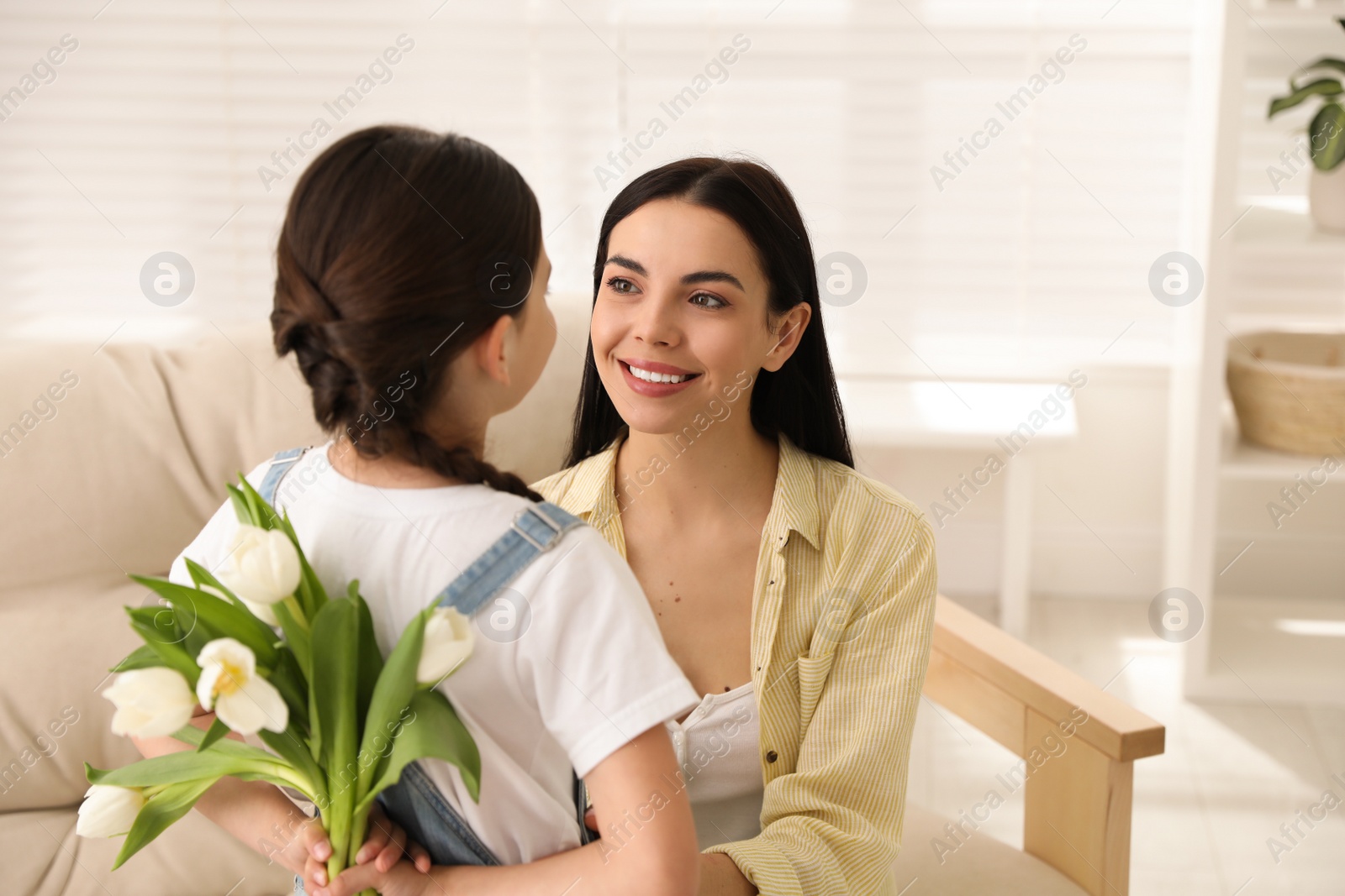 Photo of Little girl hiding tulip bouquet for mom at home. Happy Mother's Day