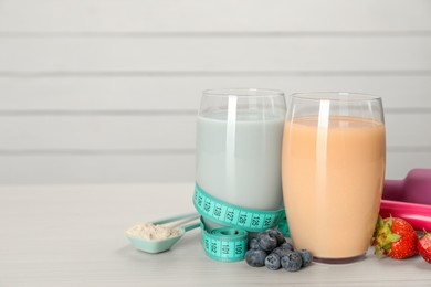 Tasty shakes with berries, measuring tape and powder on light wooden table, space for text. Weight loss