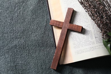 Photo of Bible, wooden cross and willow branches on color cloth, flat lay. Space for text