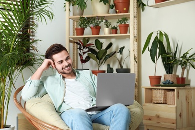 Young man using laptop in room with different home plants