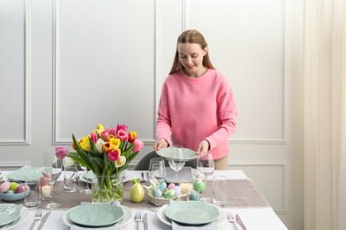 Photo of Woman setting table for festive Easter dinner at home