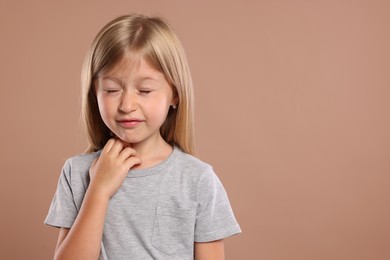 Photo of Suffering from allergy. Little girl scratching her neck on light brown background, space for text