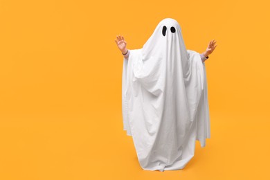 Child in white ghost costume on orange background, space for text. Halloween celebration