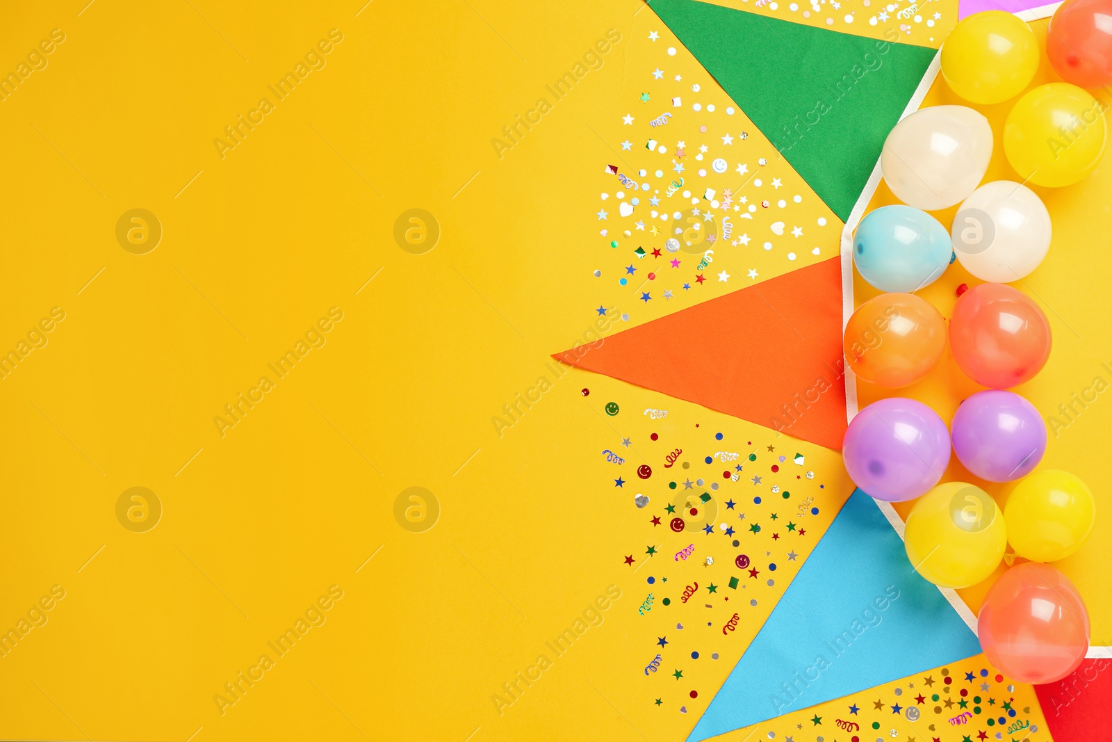 Photo of Bunting with colorful triangular flags and other festive decor on yellow background, flat lay. Space for text