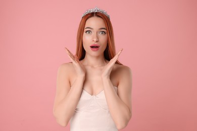 Emotional young woman with tiara on pink background, space for text