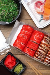 Food delivery. Delicious sushi rolls served on wooden table, flat lay