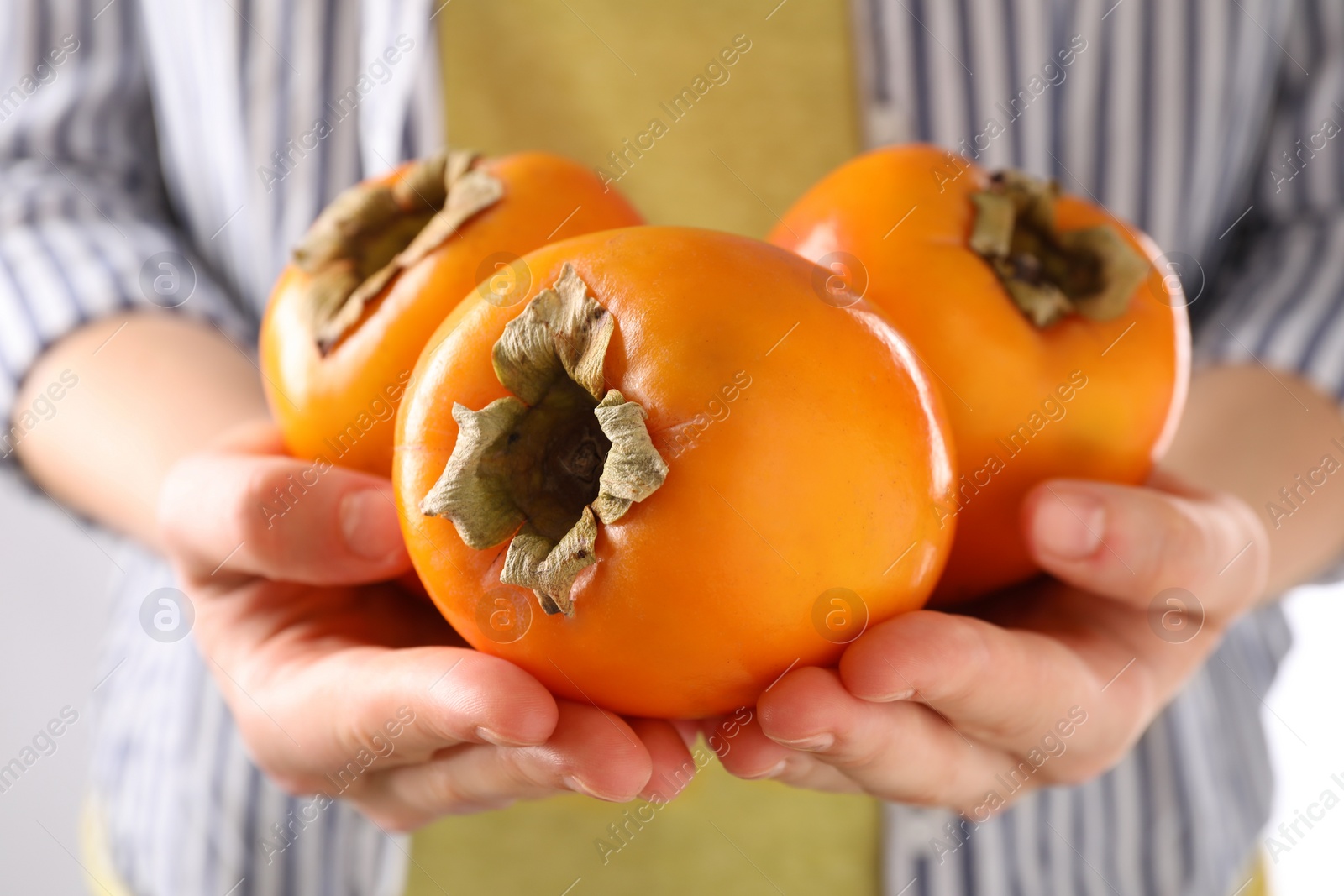 Photo of Woman holding delicious ripe juicy persimmons on light background, closeup