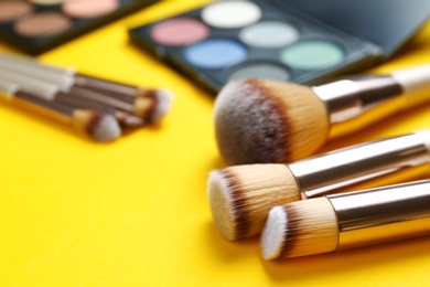 Professional makeup brushes and eye shadow palette on yellow background, space for text