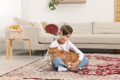 Little boy with cute ginger cat on carpet at home