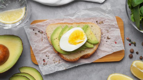 Delicious sandwich with boiled egg, pieces of avocado and basil leaves on gray table, flat lay