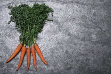 Photo of Bunch of tasty raw carrots on grey table, flat lay. Space for text