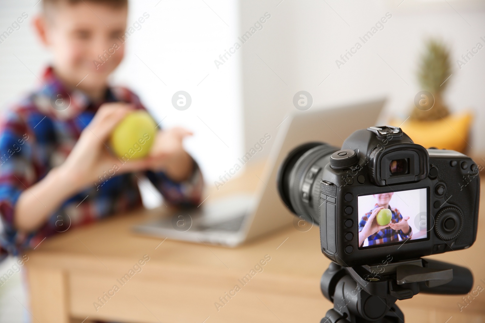 Photo of Cute little blogger with apple on camera screen, closeup