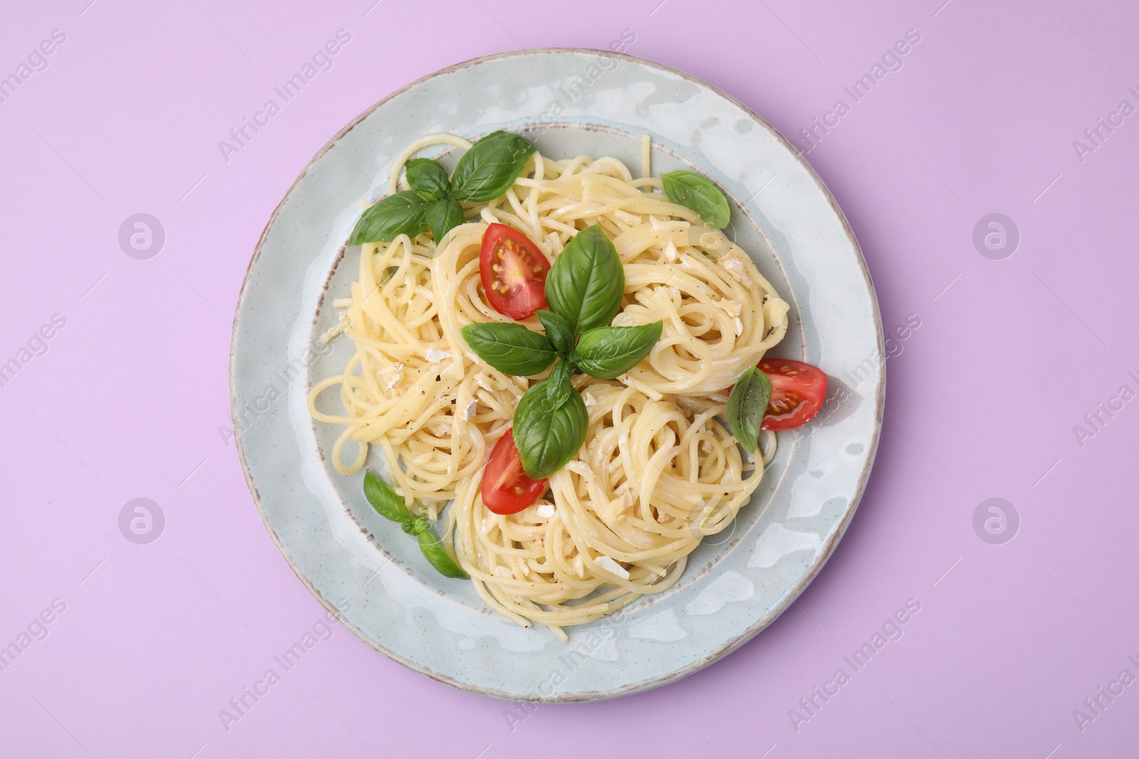 Photo of Delicious pasta with brie cheese, tomatoes and basil leaves on violet background, top view
