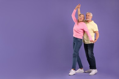 Senior couple dancing together on purple background, space for text