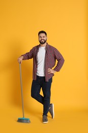 Young man with broom on orange background