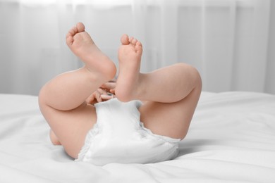 Photo of Little baby in diaper lying on bed indoors, closeup