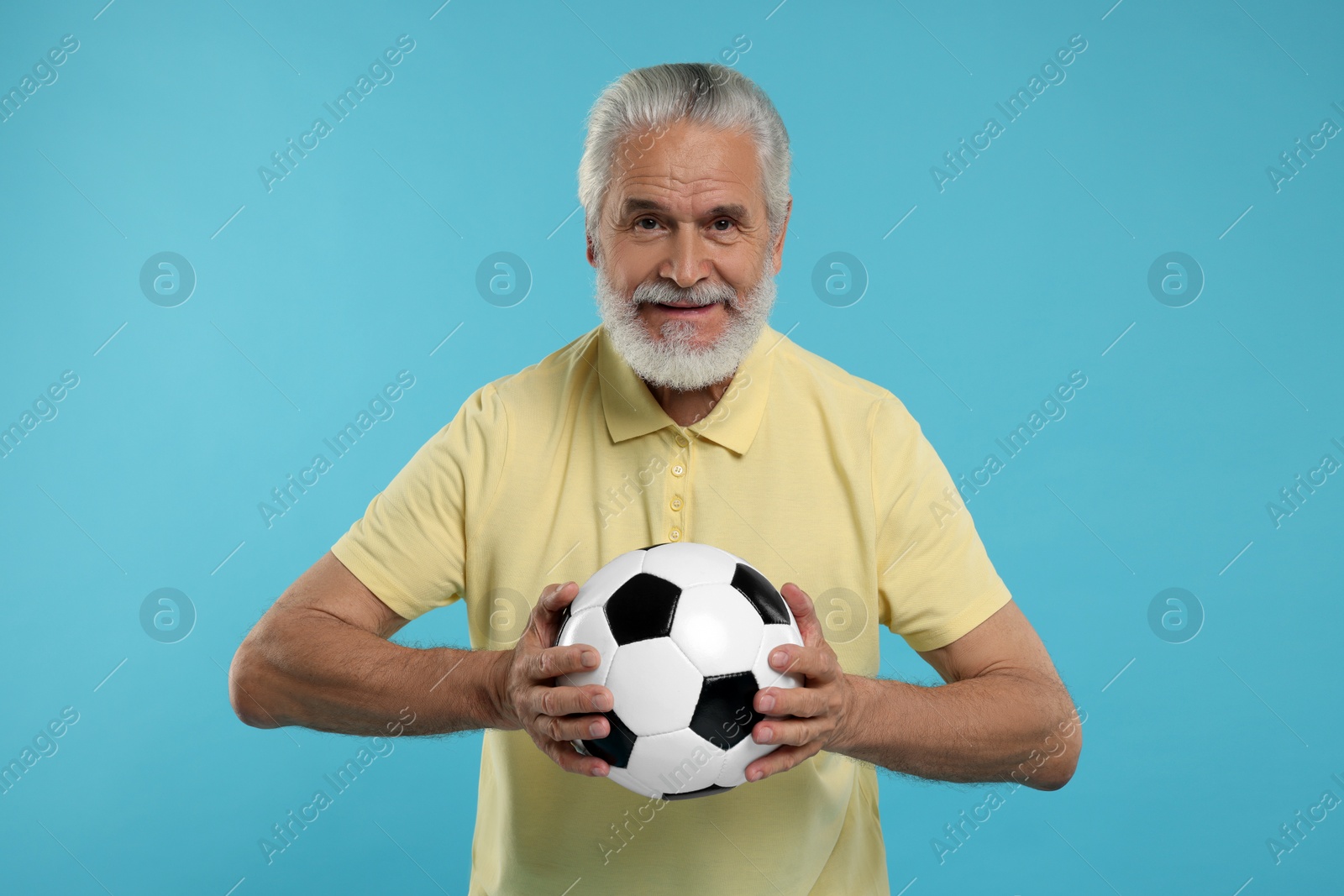 Photo of Smiling senior sports fan with soccer ball on light blue background