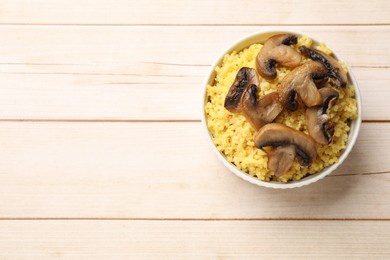 Photo of Tasty millet porridge and mushrooms in bowl on light wooden table, top view. Space for text