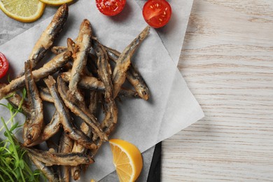 Slate board with delicious fried anchovies, lime and tomatoes on white wooden table, top view