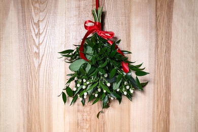 Mistletoe bunch with red bow hanging on wooden wall. Traditional Christmas decor