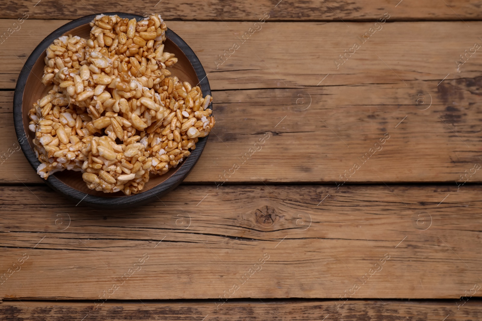 Photo of Bowl of puffed rice pieces (kozinaki) on wooden table, top view. Space for text