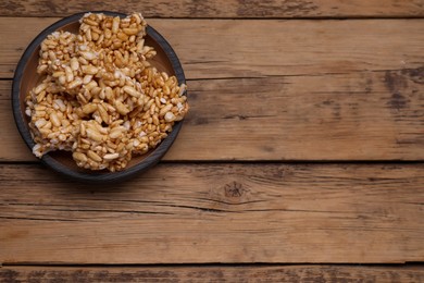 Photo of Bowl of puffed rice pieces (kozinaki) on wooden table, top view. Space for text