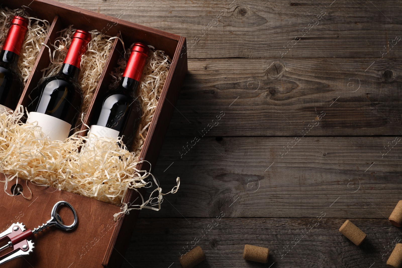 Photo of Box with wine bottles, corkscrew and corks on wooden table, flat lay. Space for text