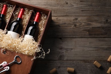 Photo of Box with wine bottles, corkscrew and corks on wooden table, flat lay. Space for text