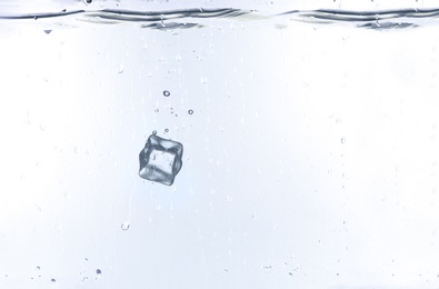 Ice cube falling into water against white background