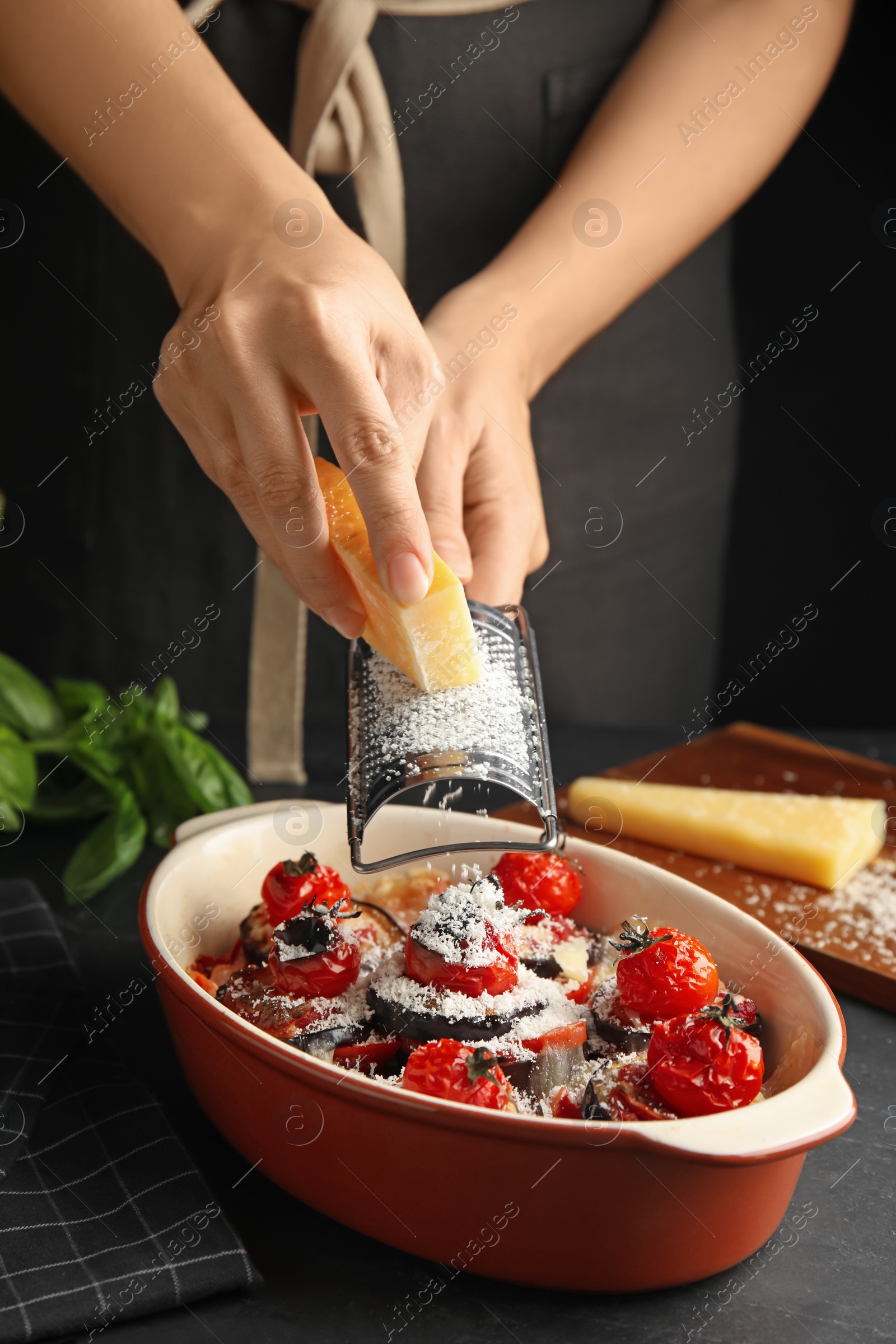 Photo of Woman grating cheese onto baked eggplant with tomatoes at table, closeup